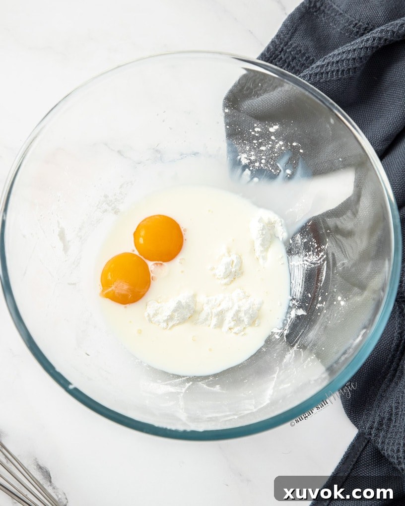 A clear glass bowl holding a mixture of egg yolks, milk, and cornflour, ready to be whisked.