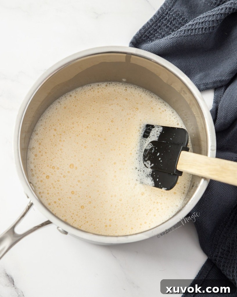 A rich, thick custard mixture bubbling gently in a saucepan over a stove.