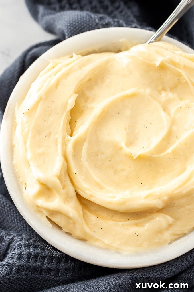 A top-down view of a glass bowl filled to the brim with smooth, yellow vanilla pastry cream, highlighting its inviting texture.