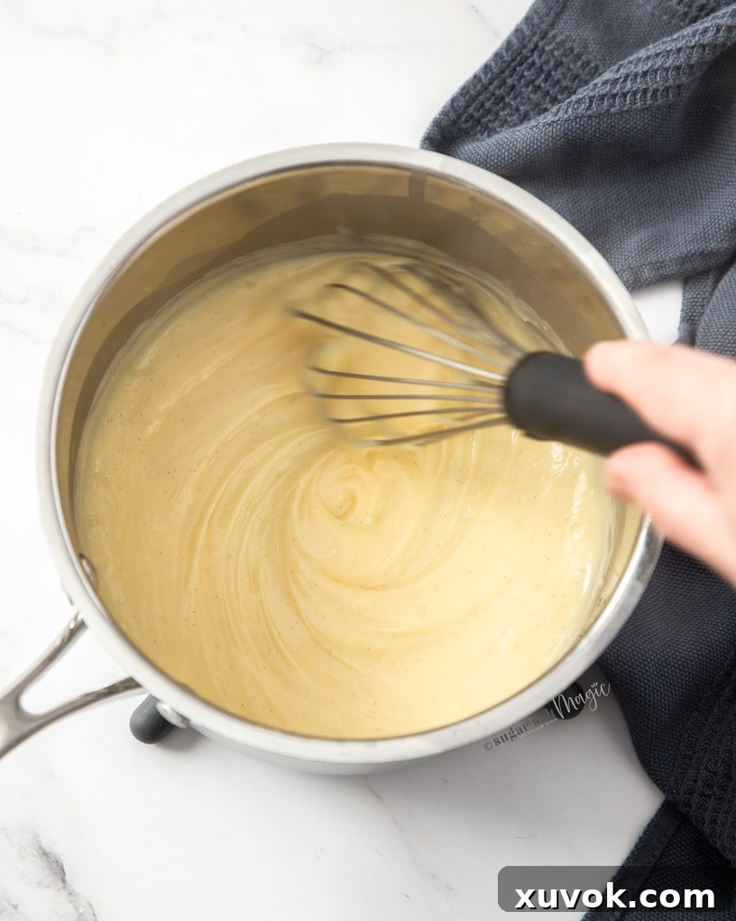 Thick pastry cream in a saucepan with a whisk in it, demonstrating the perfect consistency before cooling.