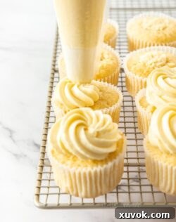 A row of cupcakes on a wire rack with frosting being piped on top