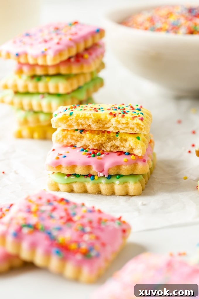 Stacks of colorfully iced sugar cookies with sprinkles on baking paper.