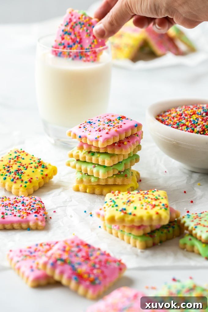 Various brightly colored iced sugar cookies covered in sprinkles on a sheet of baking paper, showcasing different decorating styles.
