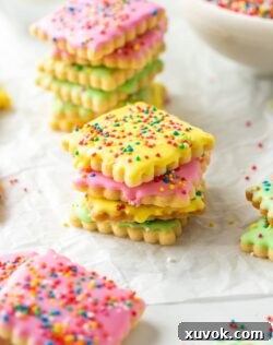 different coloured iced cookies covered in sprinkles on a sheet of baking paper