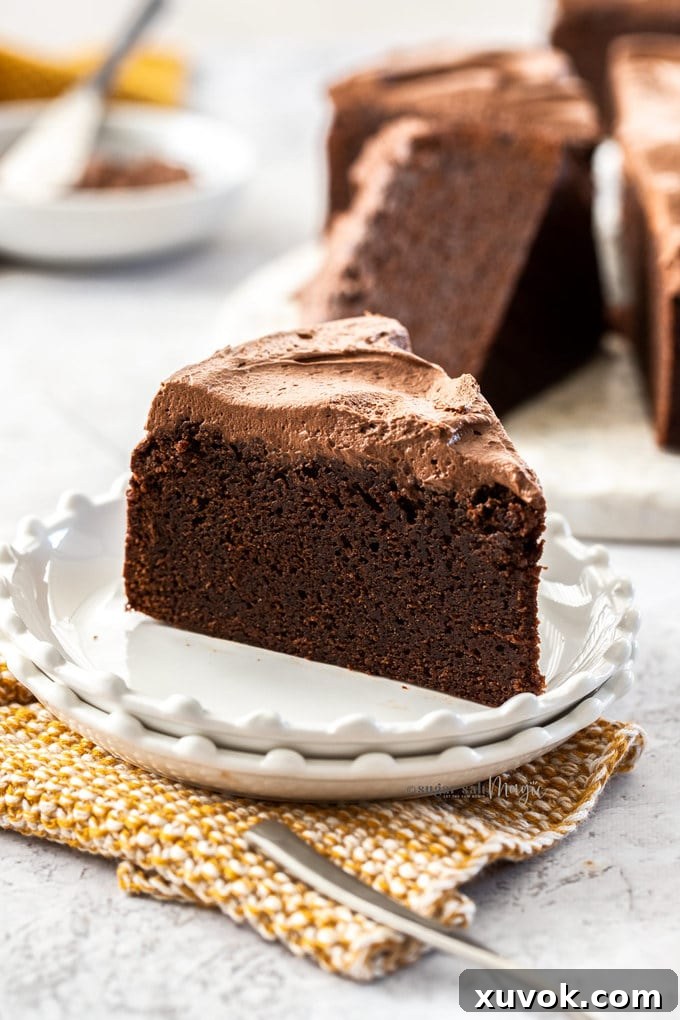 A slice of chocolate mud cake on a white plate with a mustard coloured napkin below.