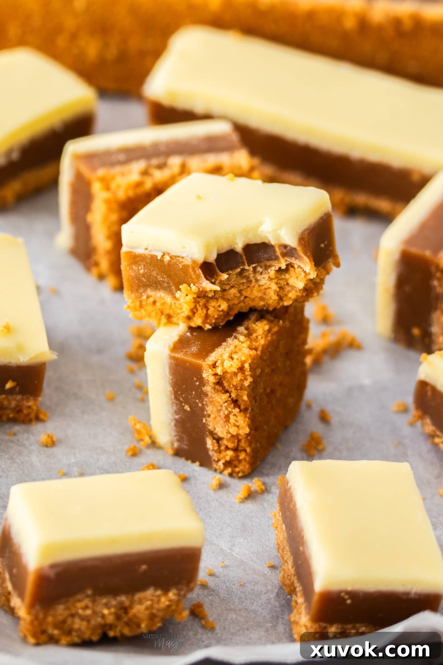 Two squares of peanut butter caramel slice, one with a bite taken out, showing the layers.