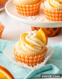 A closeup of an orange cupcake with white frosting, showing its intricate piping detail.