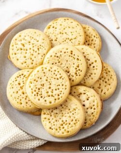A stack of golden homemade crumpets on a rustic grey plate, ready to be served and enjoyed.