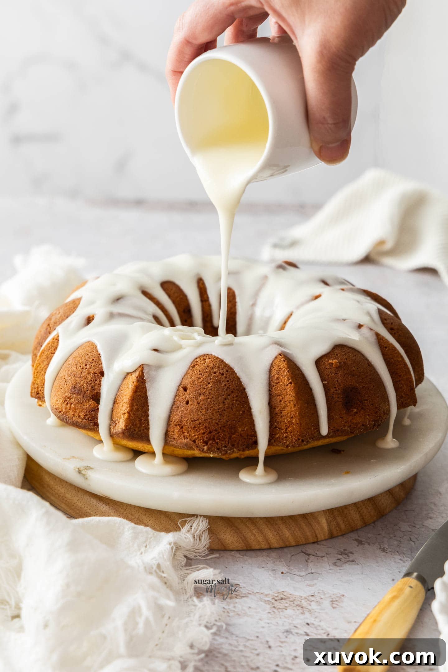 Thick lemon icing gracefully pouring from a jug onto a beautifully fluted bundt cake, creating tempting drizzles down the sides.