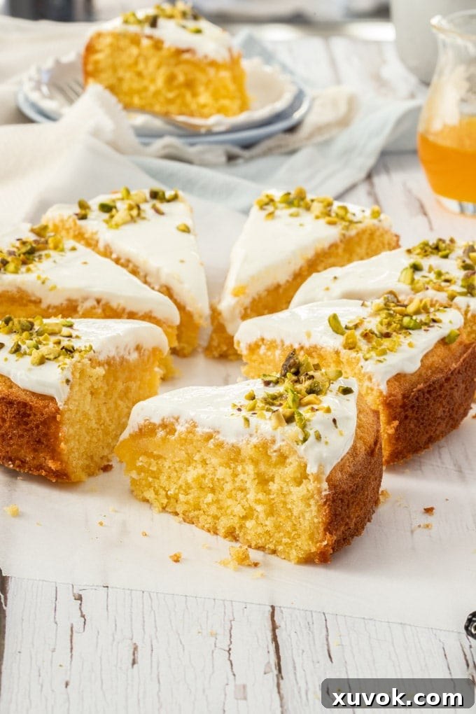 Greek Orange Semolina Cake sliced up, sitting on a piece of baking paper, one slice is on a plate in the background.