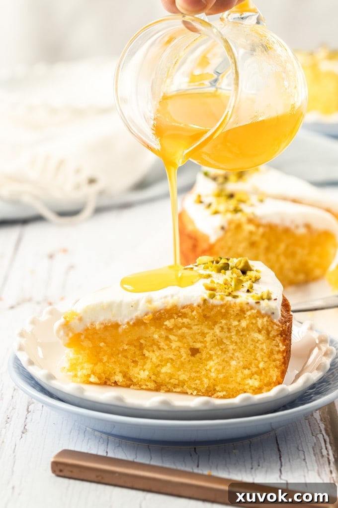 Pouring orange syrup over a slice of cake on a white plate.