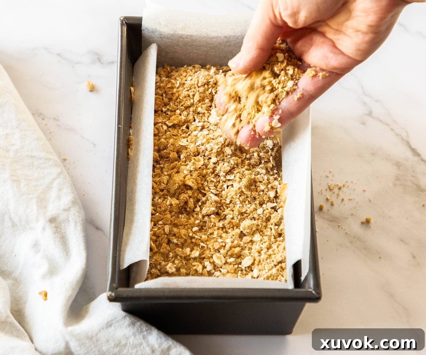 A hand scattering streusel over the top of cake batter in a loaf pan.
