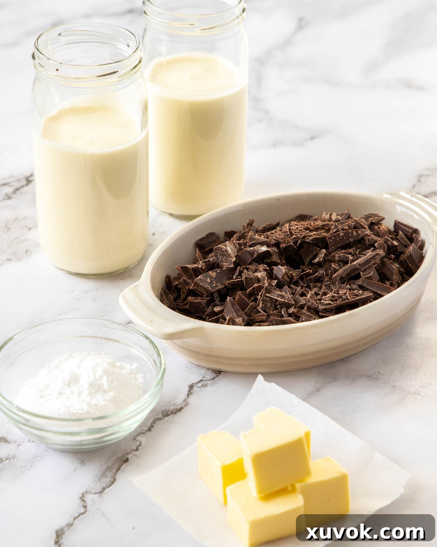 Ingredients for easy chocolate mousse on a marble benchtop including dark chocolate, butter, powdered sugar, and a carton of heavy cream.