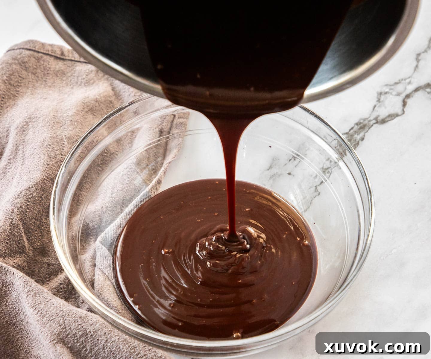 Pouring the chocolate mixture from a saucepan into a glass bowl.