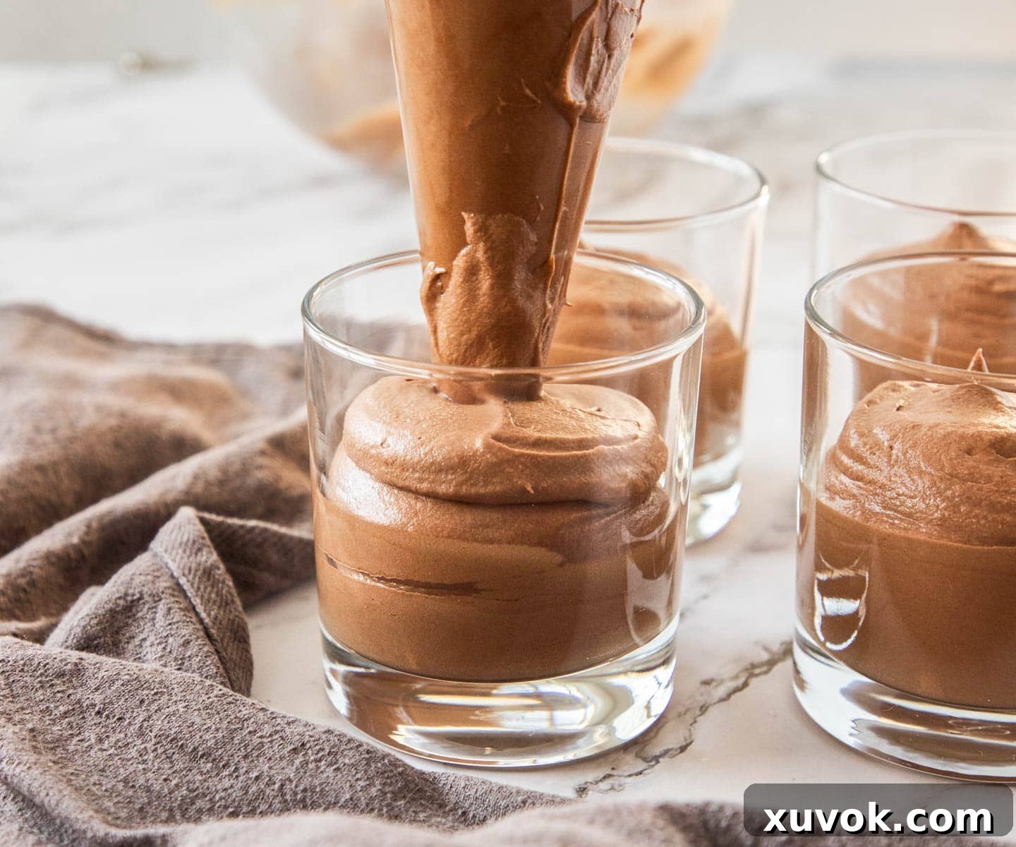 Piping the chocolate mousse into small glasses for serving.
