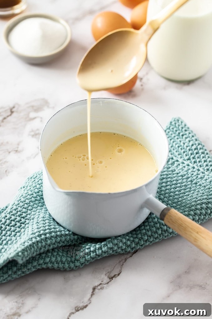 A small, elegant white saucepan filled with a perfectly smooth, pale yellow vanilla sauce (crème anglaise), ready for serving.