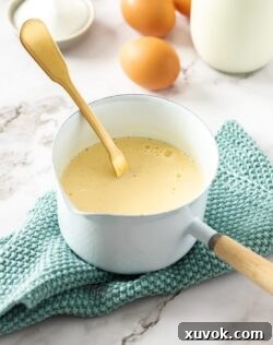 A small white saucepan filled with crème anglaise, highlighting its smooth, pale yellow color and ready-to-pour consistency.