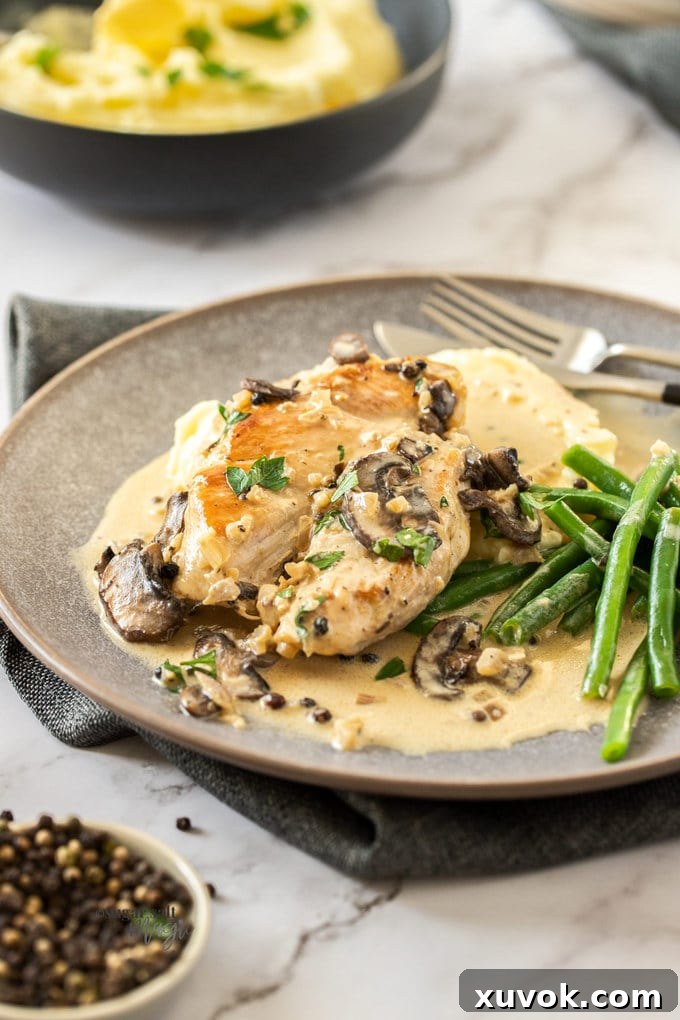 Peppercorn chicken breast sitting on top of mashed potato on a grey plate.