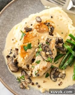 Top down view of peppercorn chicken sitting on top of mashed potato on a grey plate