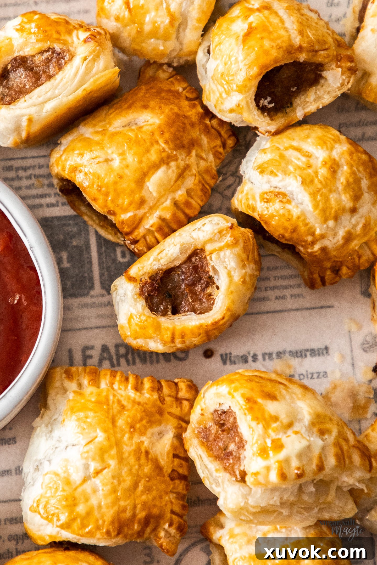 Closeup of a mini sausage roll, showing its golden-brown, flaky pastry and savory filling.