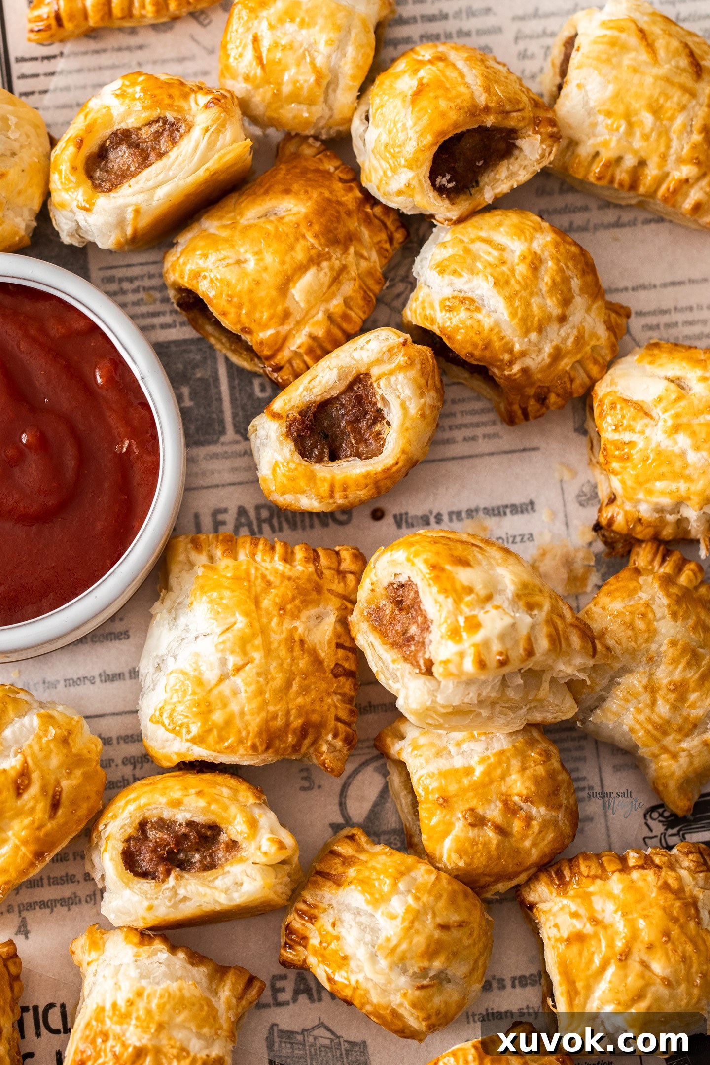 Top-down view of a freshly baked batch of golden-brown sausage rolls, arranged on a baking sheet.