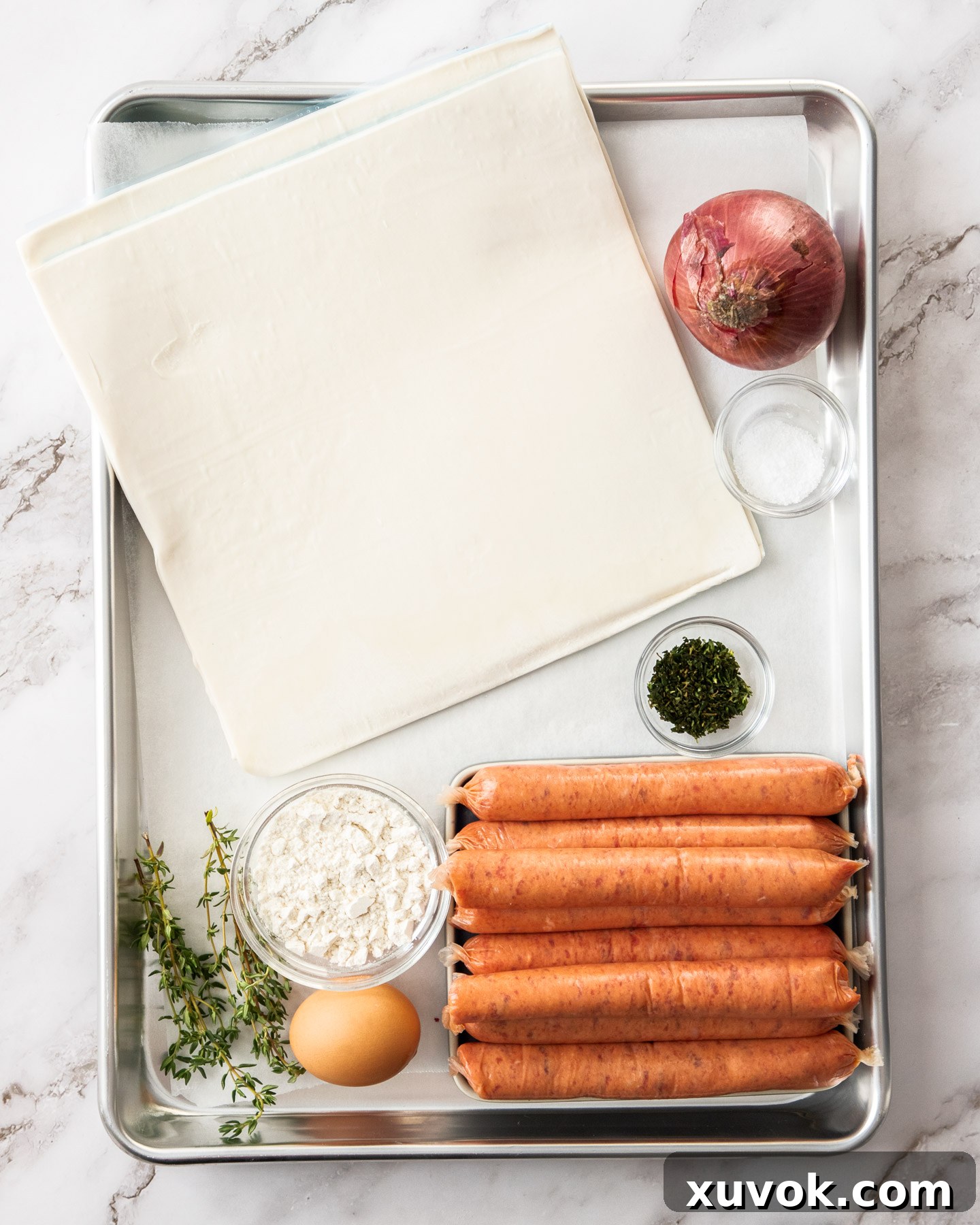 Ingredients for beef sausage rolls neatly arranged on a baking tray, ready for preparation.