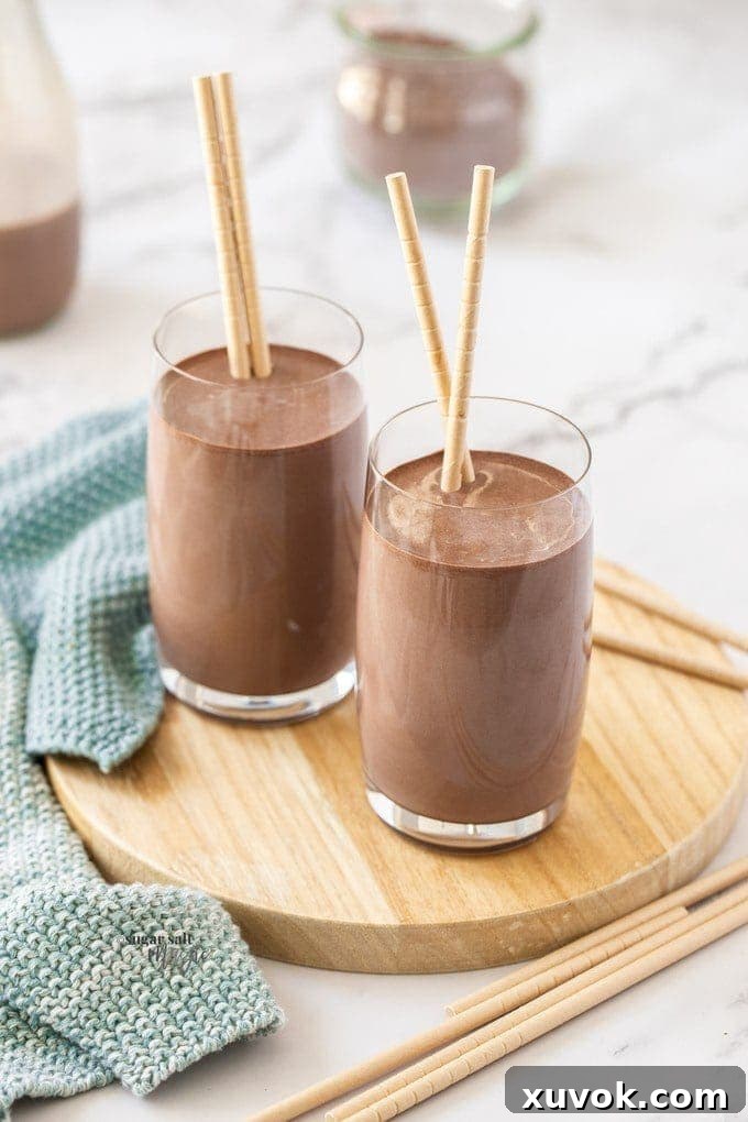 2 glasses of homemade chocolate milk sitting on a small wooden platter, garnished with chocolate shavings