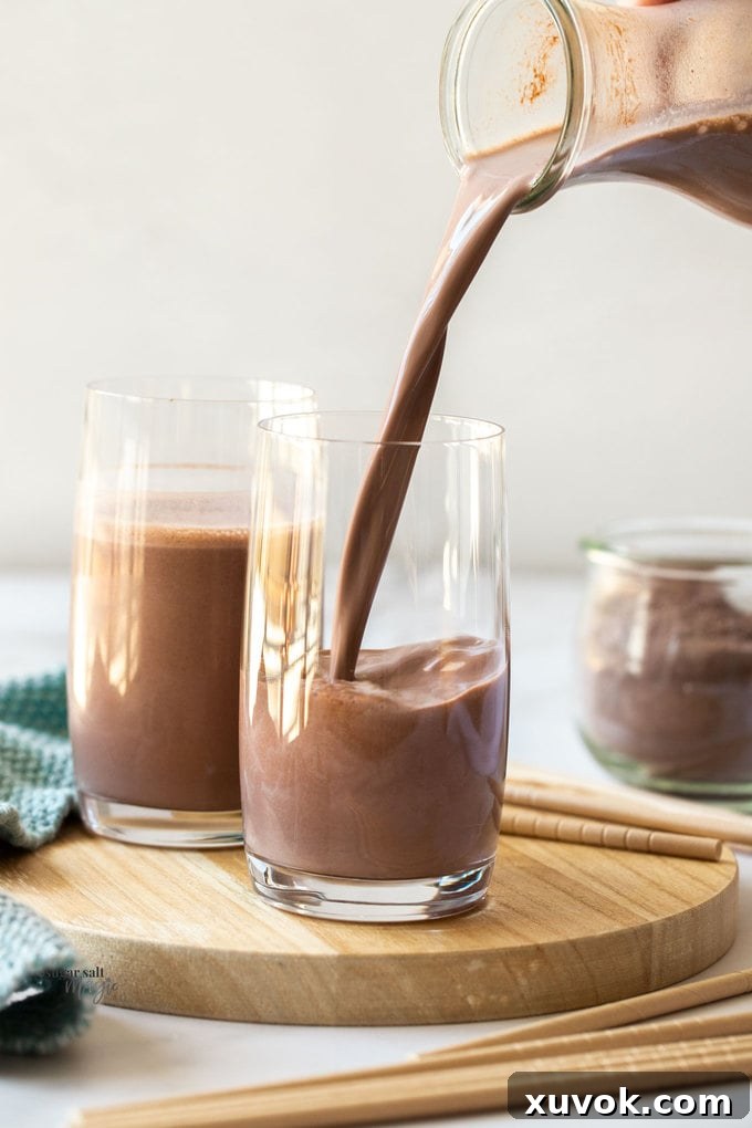 Rich chocolate milk being poured from a pitcher into a tall glass, creating a luscious cascade