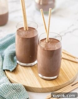 2 glasses of homemade chocolate milk sitting on a small wooden platter, garnished with chocolate shavings