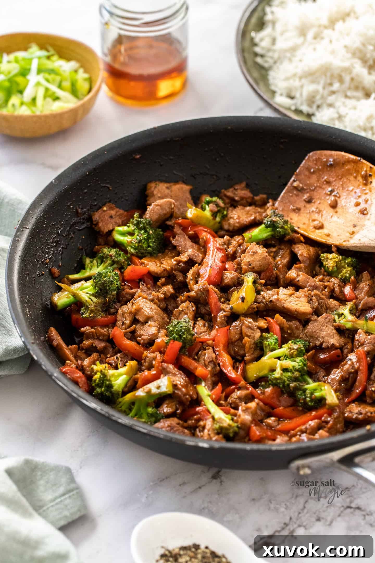 A black pan filled with vibrant honey pepper pork stir fry, showcasing tender pork strips and colorful vegetables, ready to be served.