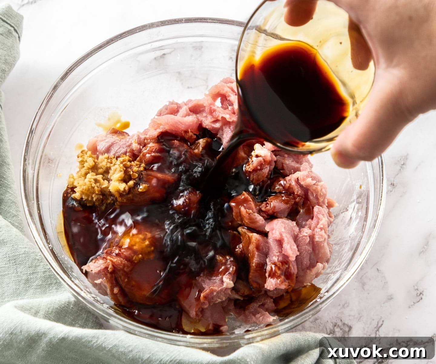 Pork strips being mixed with a vibrant marinade in a bowl, with soy sauce being poured over for added flavor.