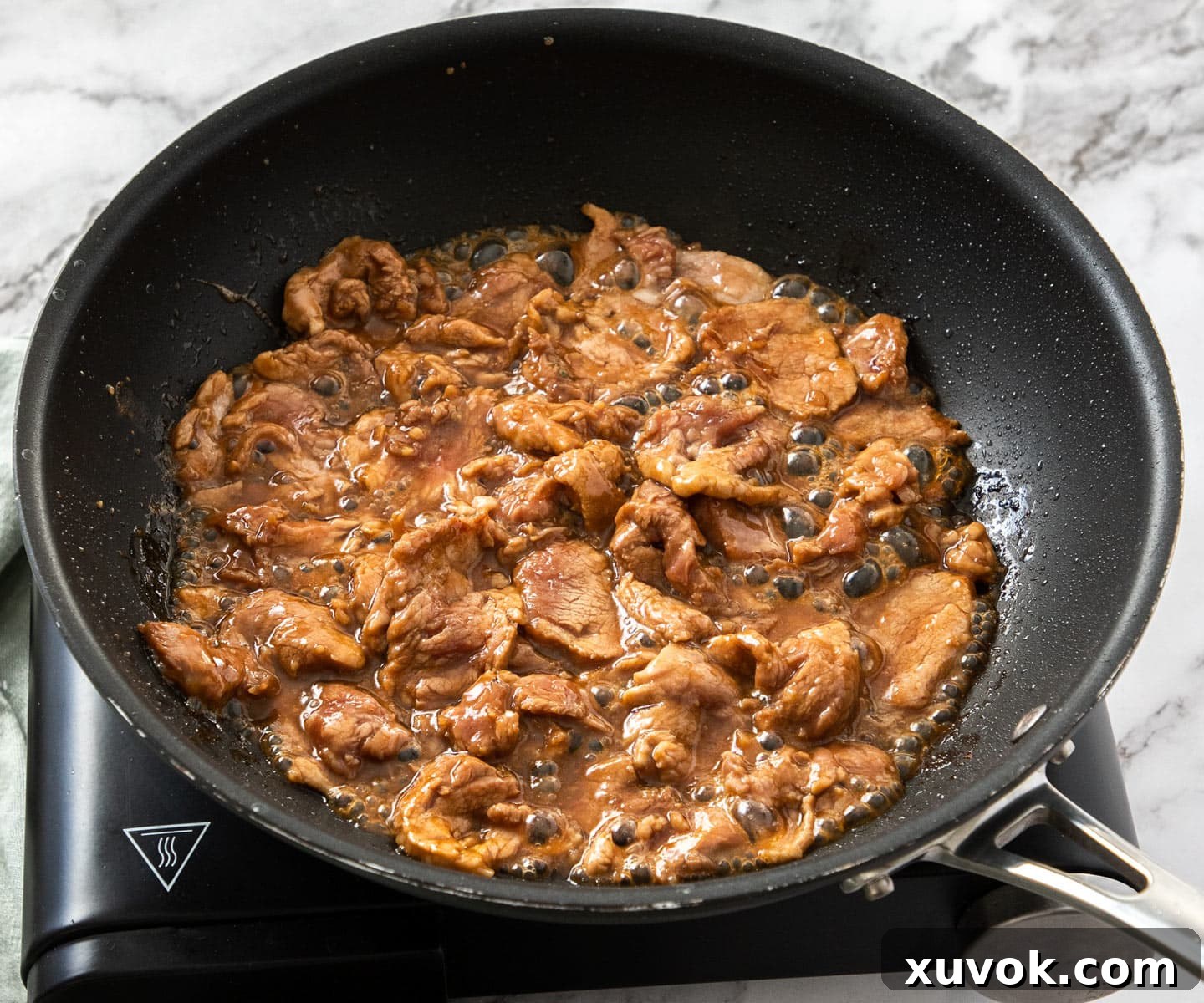 Pork strips frying and sizzling in a hot pan, demonstrating the searing process.