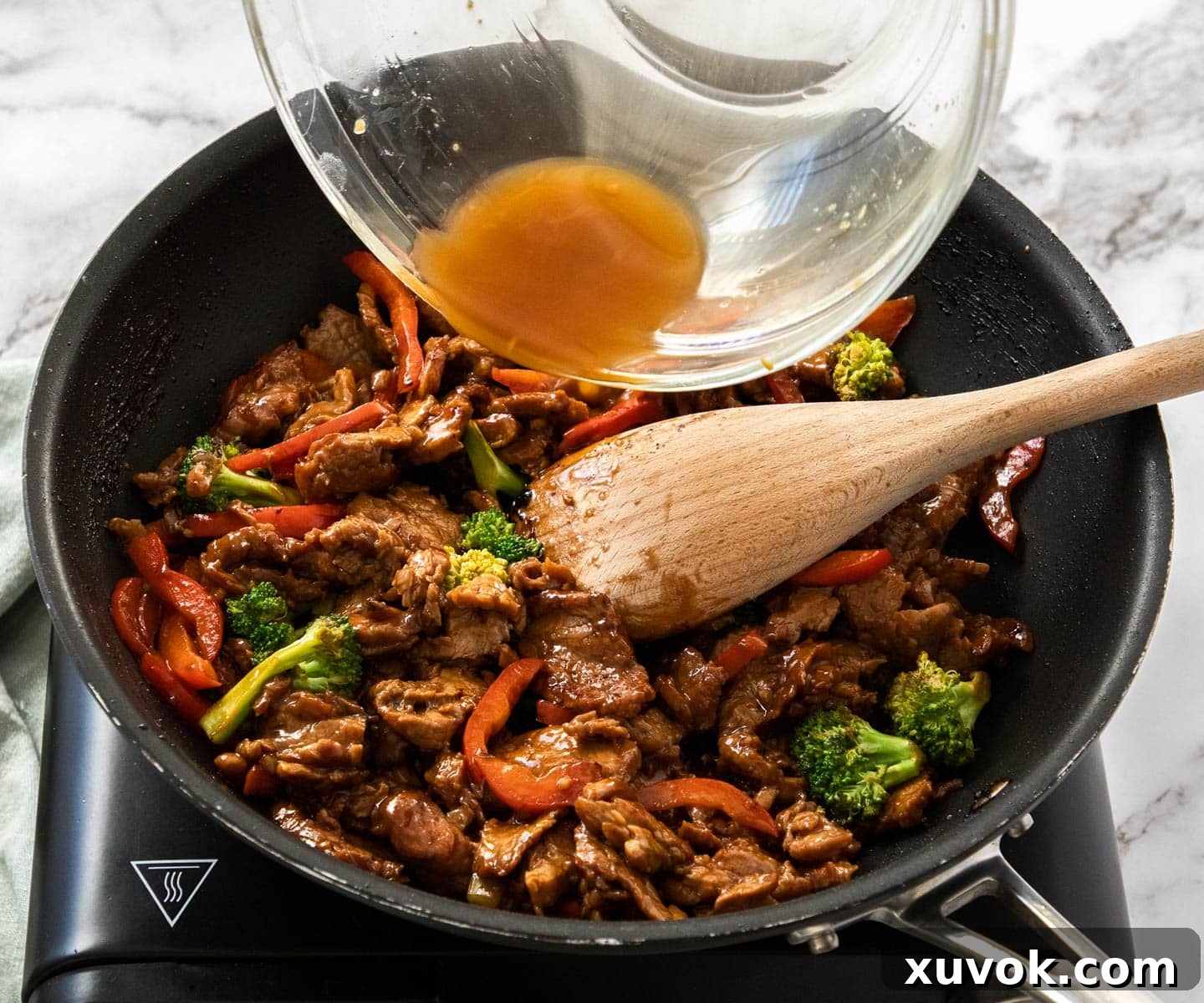 Adding the thickened sauce to the stir-fried vegetables and pork in a pan, illustrating the final combining step.