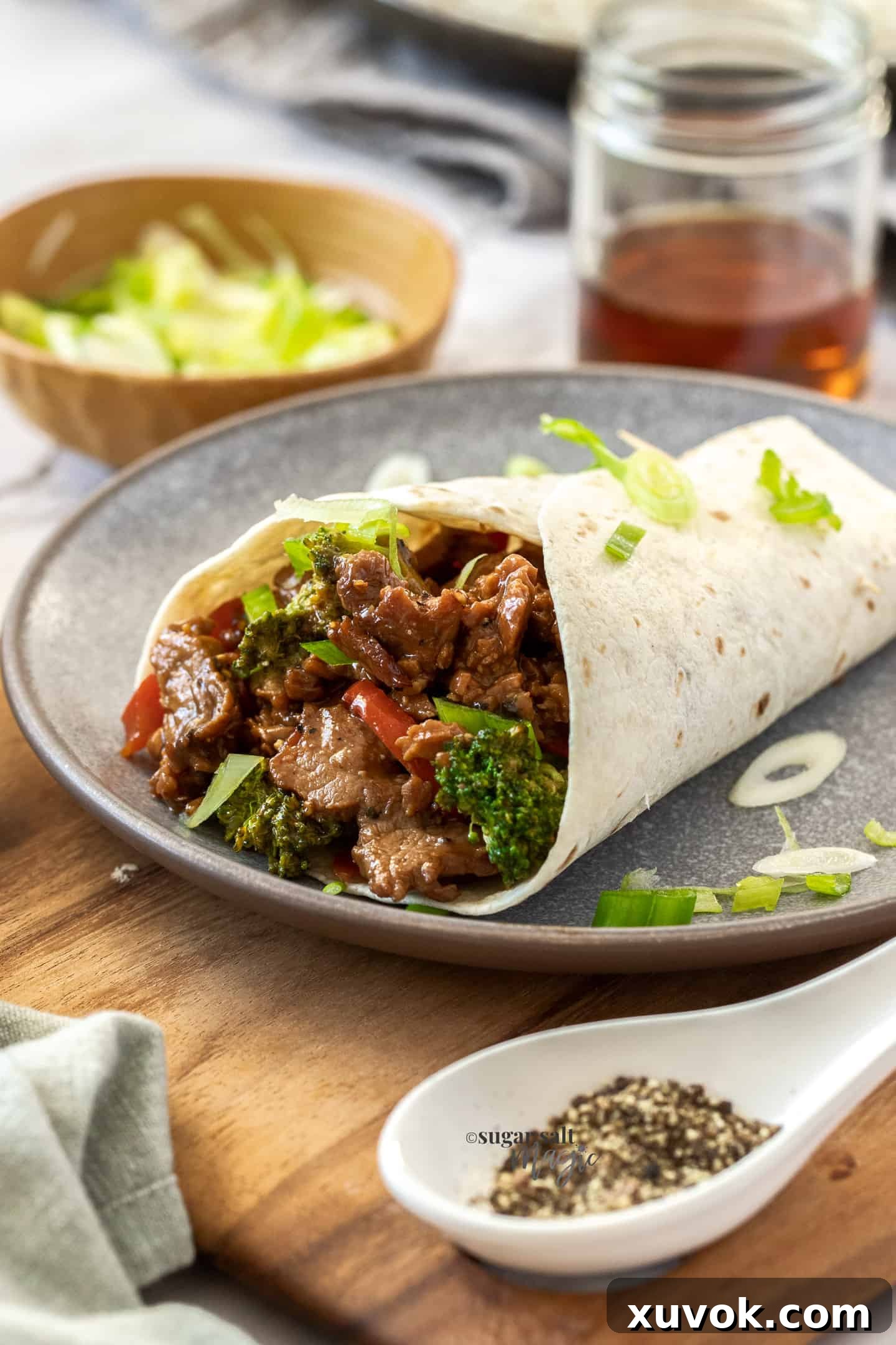 Honey pepper pork stir fry served creatively in a soft tortilla on a grey plate, garnished with spring onions.