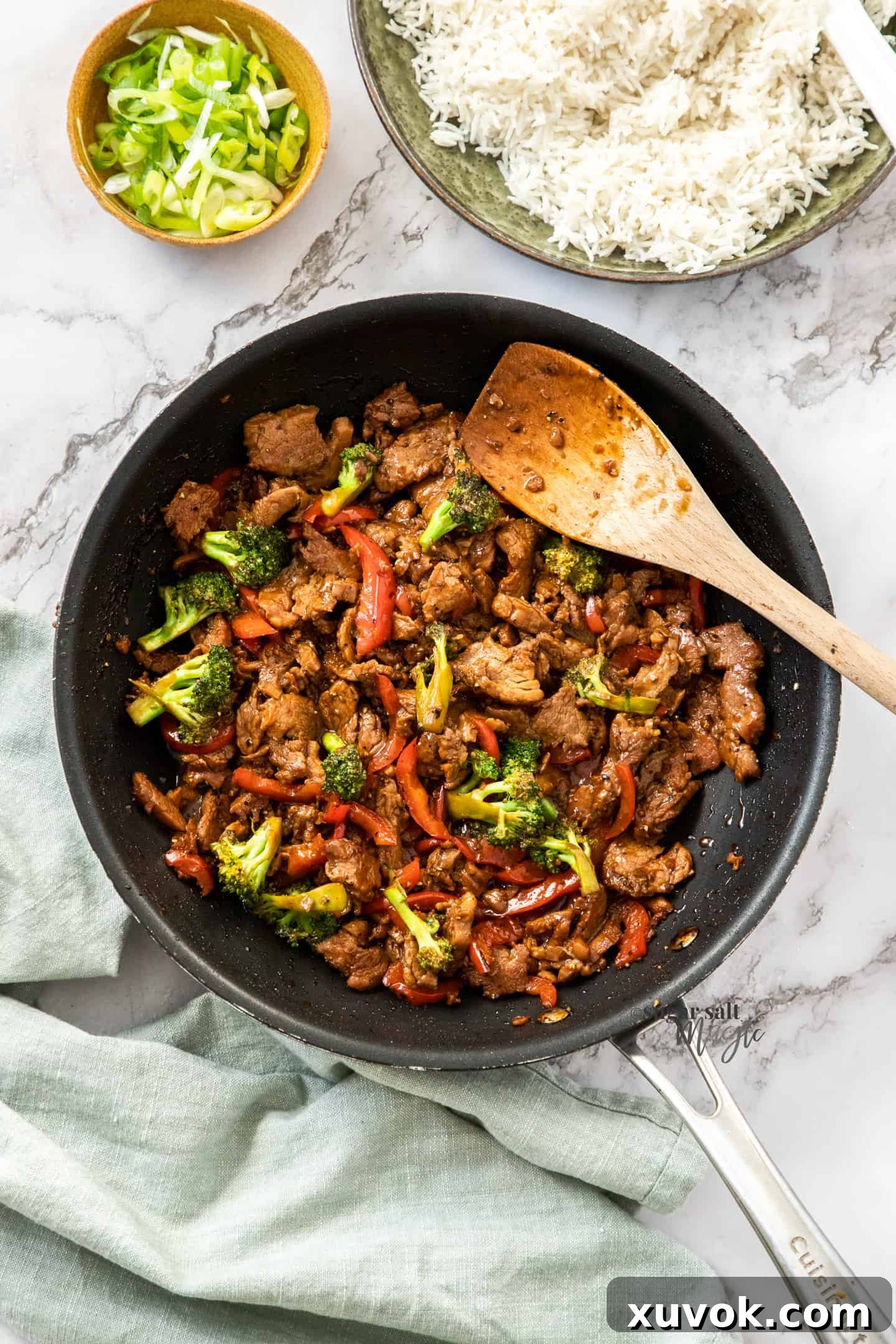 A black pan brimming with a generous serving of beautifully cooked honey pepper pork stir fry, vibrantly garnished with fresh spring onions.