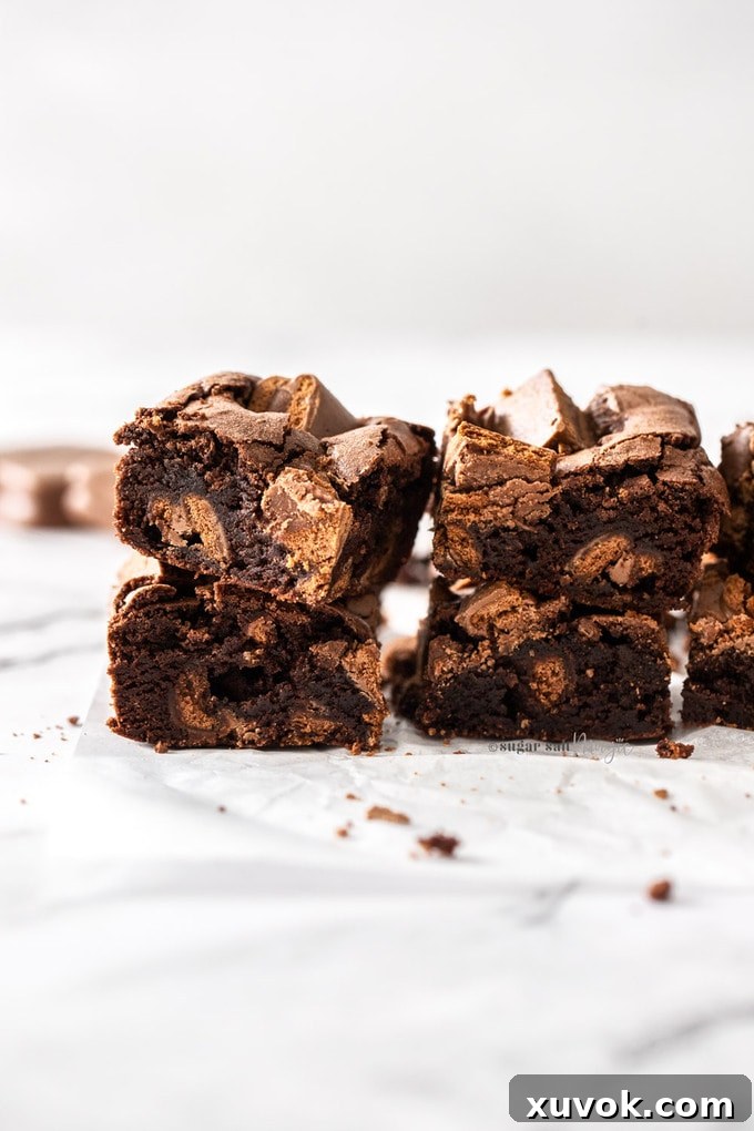 Two enticing stacks of Tim Tam brownies resting on a sheet of white baking paper, highlighting their thick, fudgy texture and delicious topping.