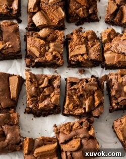 Top down view of a batch of 16 brownies on a sheet of white baking paper