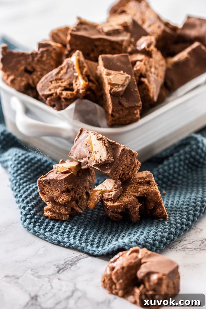 Stacked Milo Mars Bar Slices with a full pan of treats in the background.