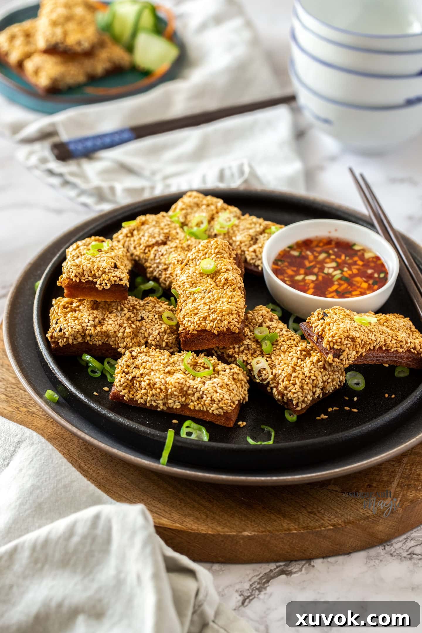 A batch of prawn toast on a black plate with a white bowl filled with chilli sauce, ready to be served as a delicious appetizer.