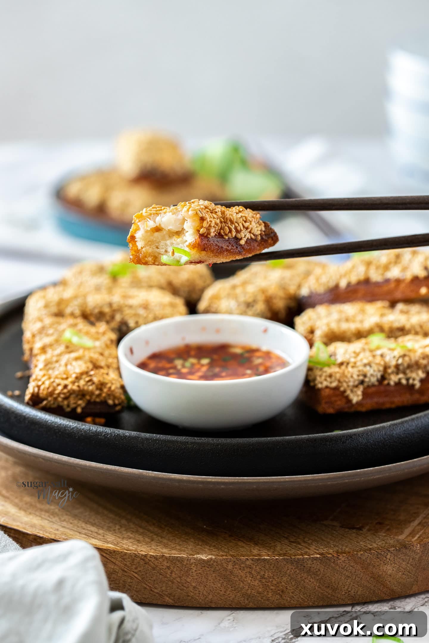 Chopsticks holding a slice of sesame prawn toast, revealing the succulent prawn filling inside its crispy shell.