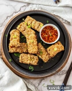 A batch of prawn toast on a black plate with a white bowl filled with chilli sauce, ready to be served.
