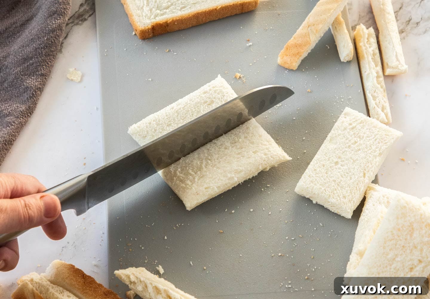A knife neatly cutting a slice of white bread in half, preparing it for prawn toast.