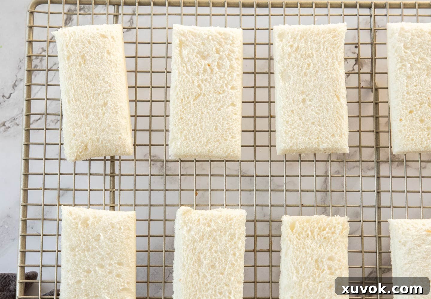Slices of white bread neatly arranged on a wire rack, drying out overnight for optimal crispness in prawn toast.