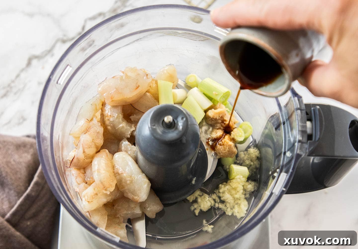 A hand pouring light soy sauce into a food processor containing prawns and other ingredients for the filling.