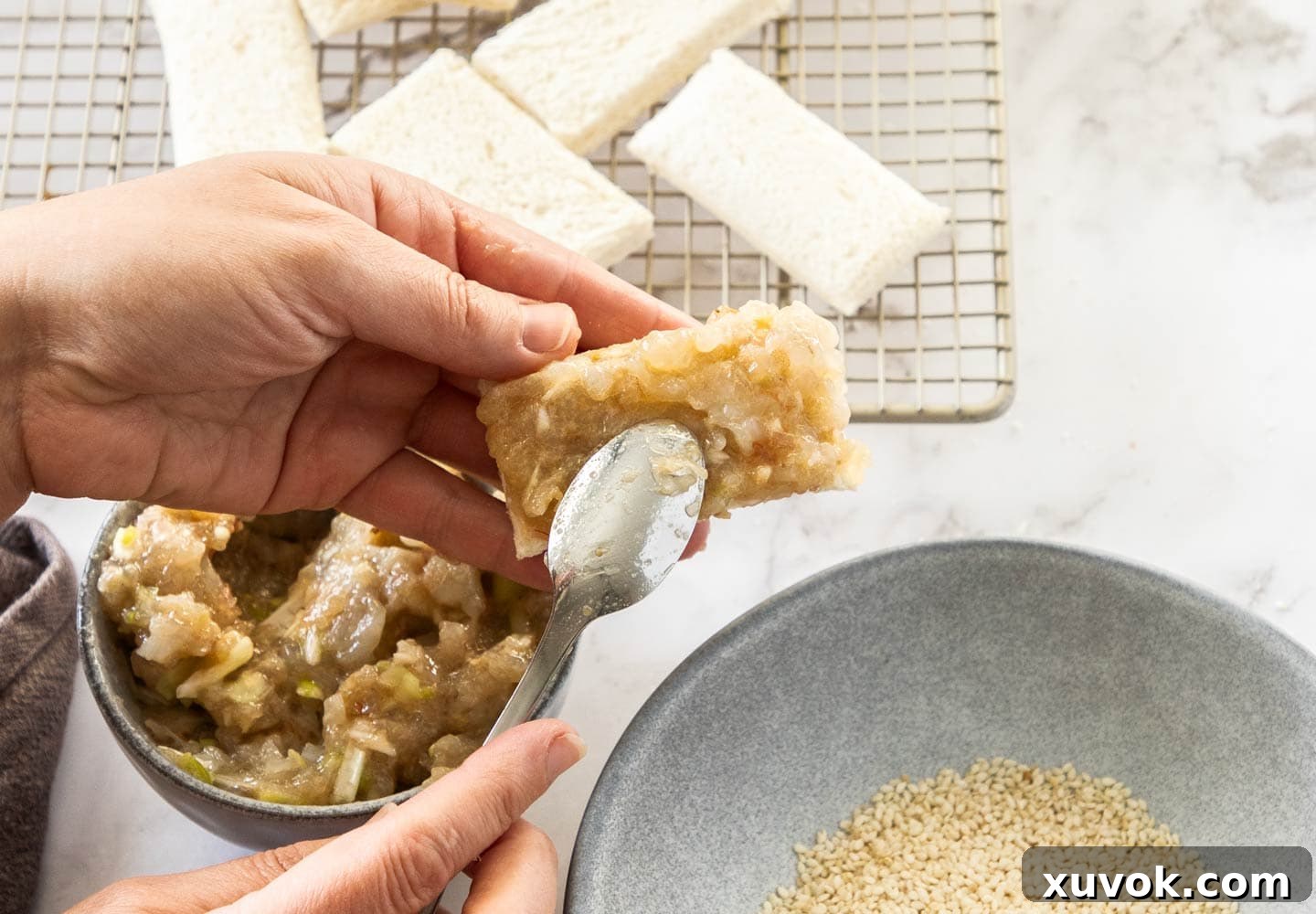 A hand spreading a thick layer of prawn paste evenly onto a piece of white bread.