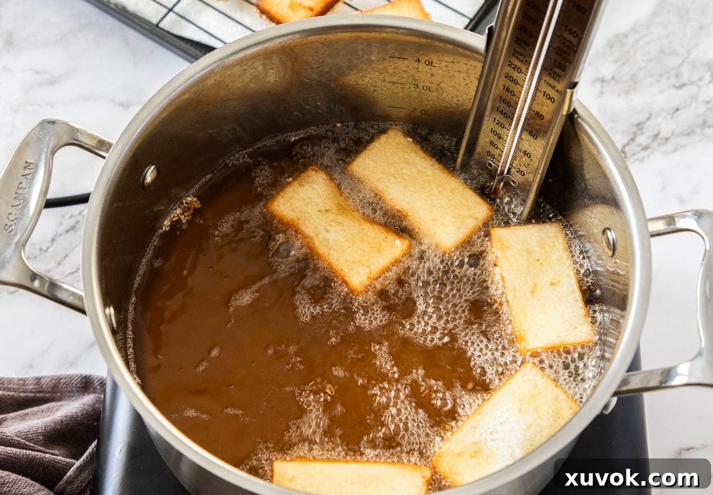 Several pieces of prawn toast frying in hot oil in a deep saucepan, turning golden brown.