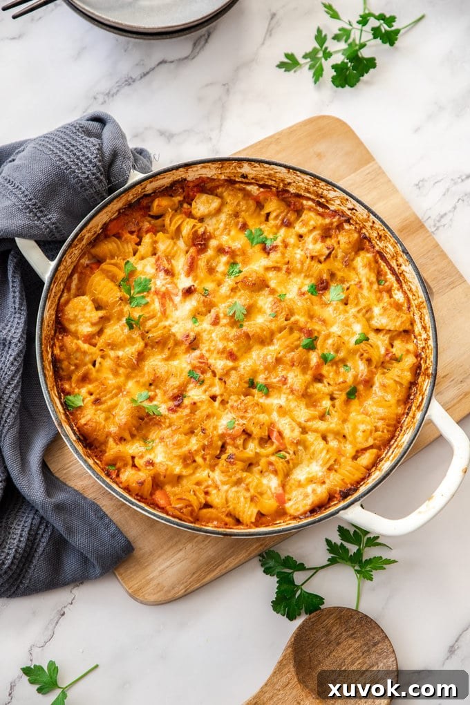 Top down view of pasta bake in a white enamel pan on a wooden board, with grey tea towel next to it.