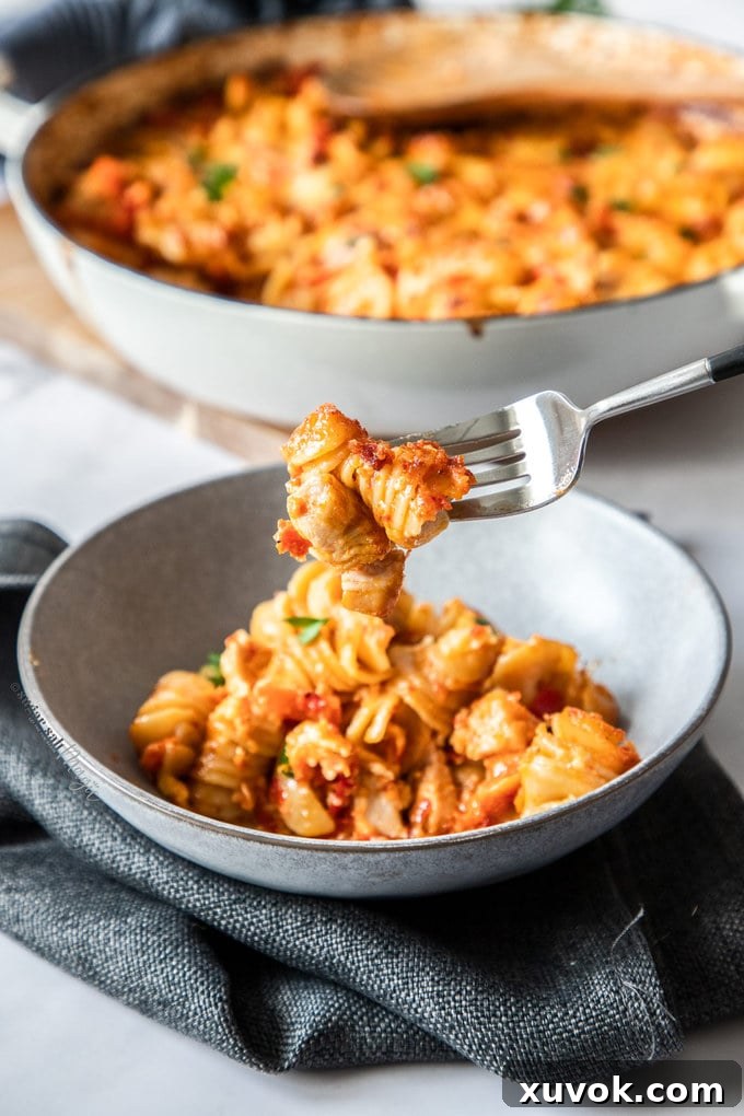Pasta bake in a grey bowl, sitting on a dark grey napkin. 