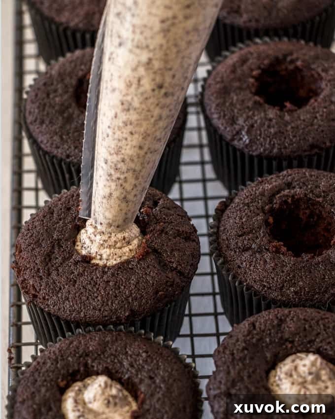 Filling scooped-out chocolate cupcakes with a creamy cookies and cream filling, preparing them for the top layer of frosting.