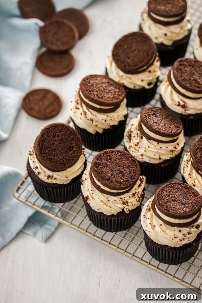 A batch of freshly baked chocolate cookies and cream cupcakes, each adorned with white frosting and a cookie on top.
